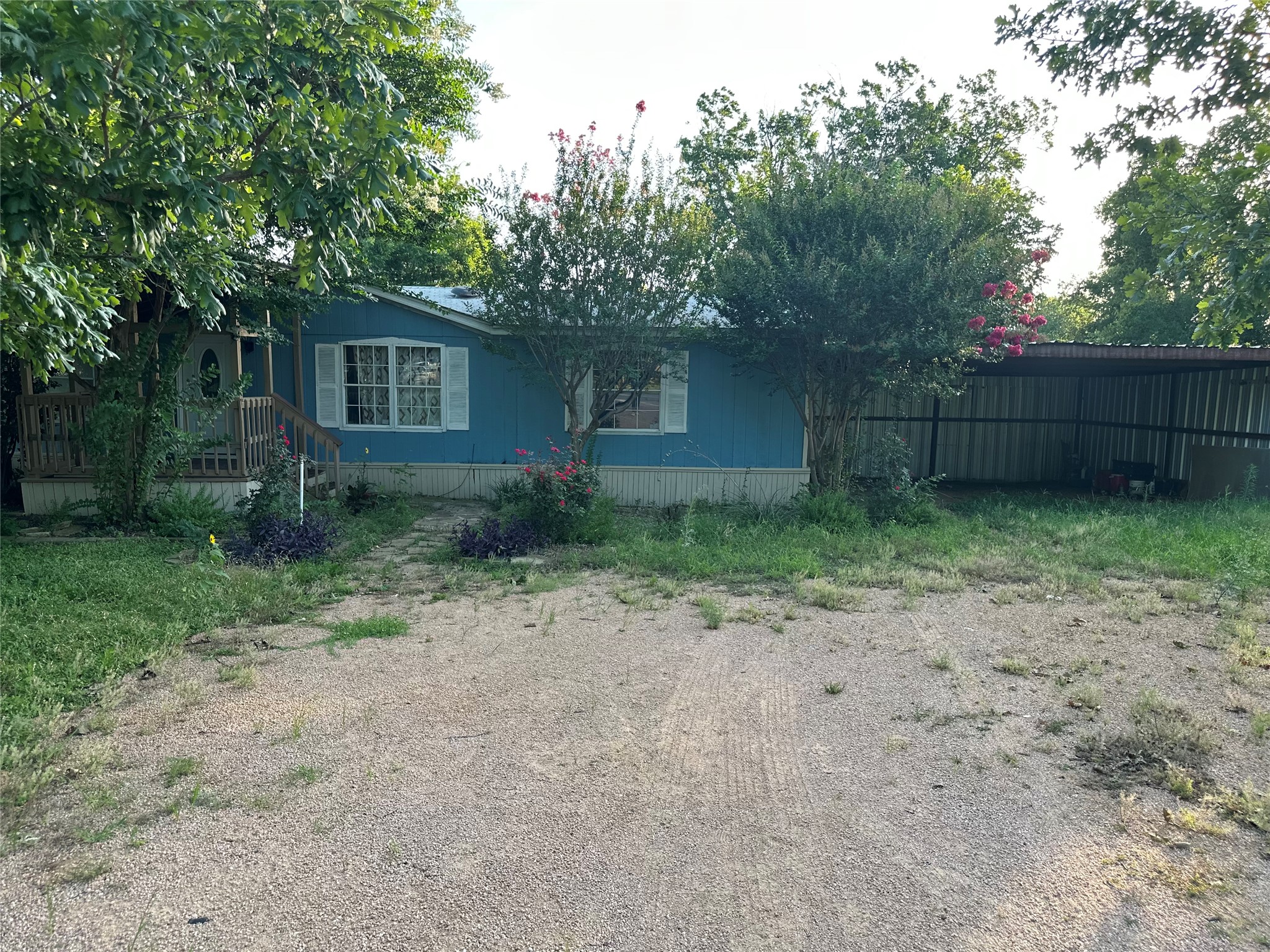A charming blue home with white trim offers a welcoming porch and abundant green landscaping.
