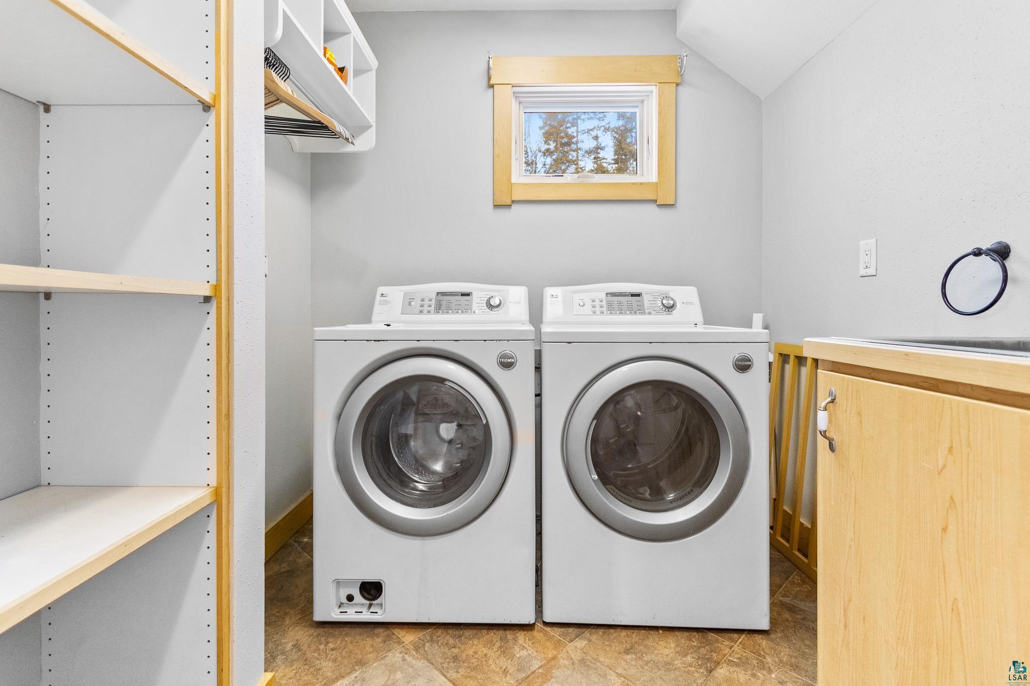 5163 Greenwood Road Duluth, MN 55804 - Photo 40 of 47 Laundry area featuring side-by-side front-load appliances, a utility sink with wood-finish cabinetry, a window with natural wood trim, and built-in shelving with hanging rod