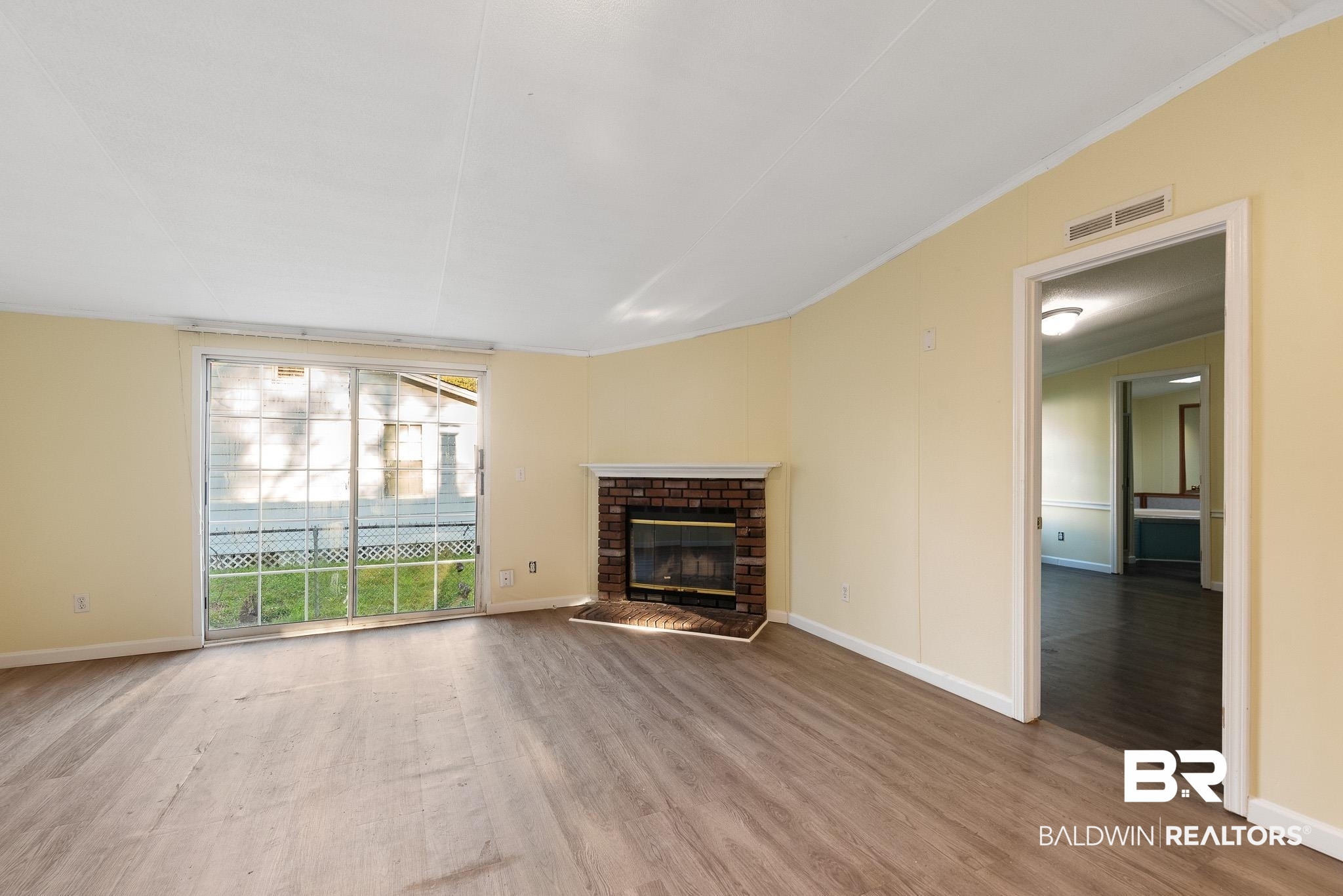 7695 Bermuda Drive Semmes, AL 36575 - Photo 8 of 27 Unfurnished living room featuring a brick fireplace, wood finished floors, visible vents, and baseboards