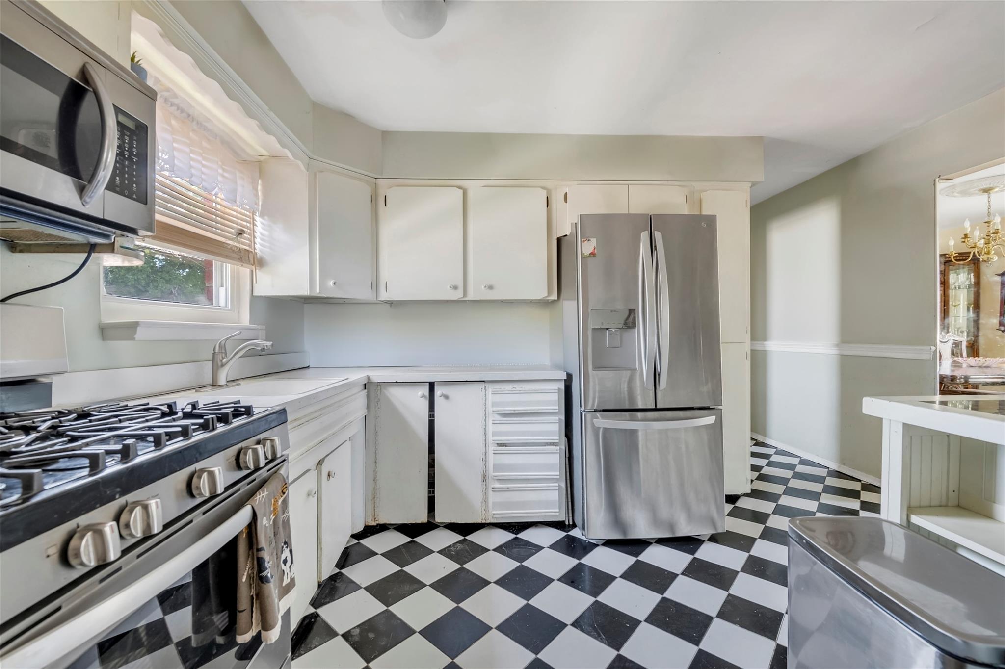 Kitchen featuring stainless steel appliances, dark flooring, light countertops, white cabinetry, and a chandelier