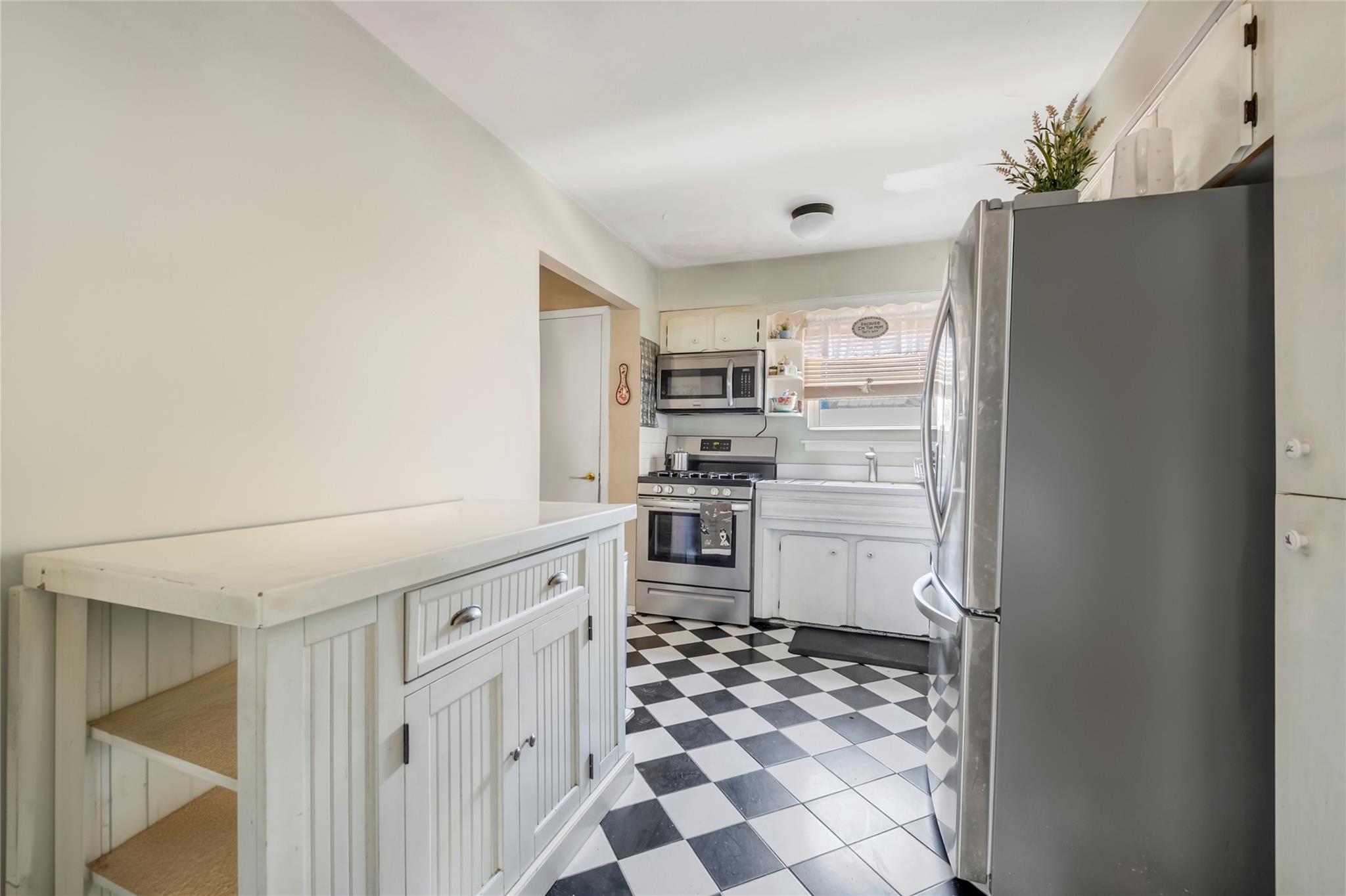 Kitchen with stainless steel appliances, dark floors, light countertops, white cabinets, and open shelves