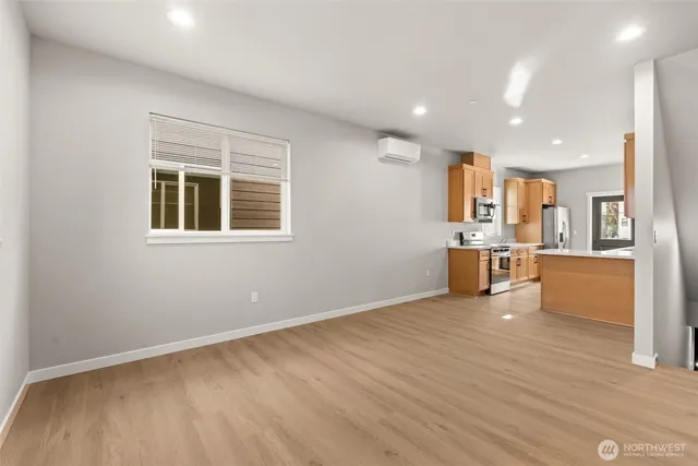 a view of empty room with wooden floor and kitchen view