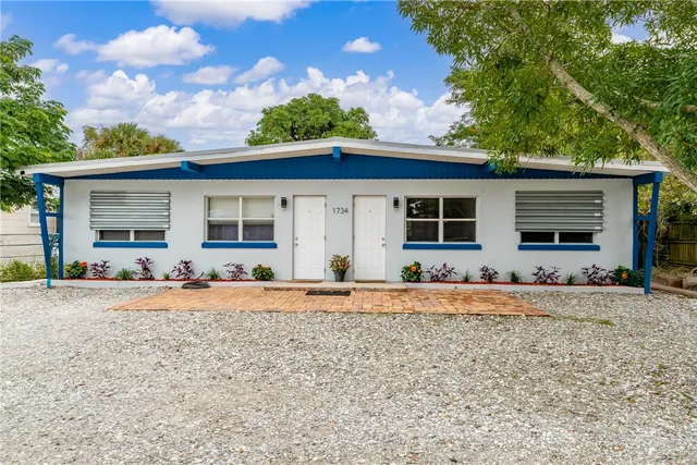 a front view of a house with a dirt yard and a large tree