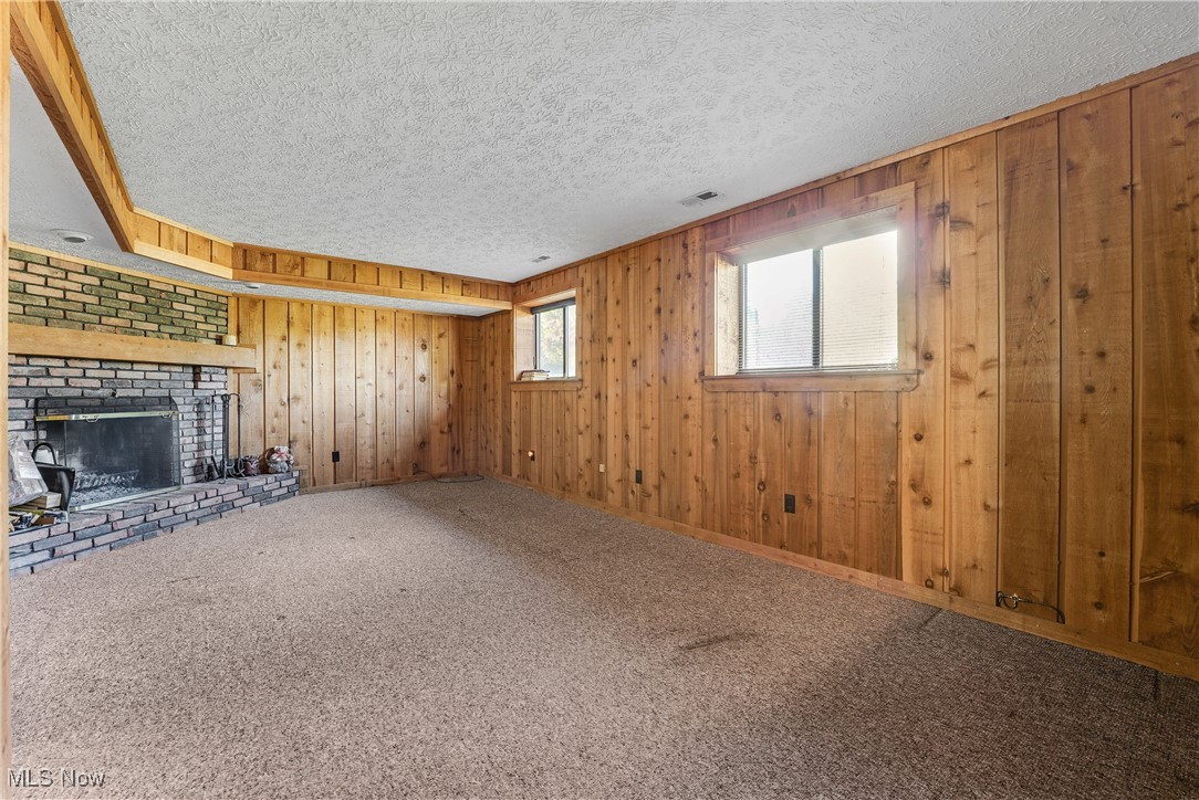 123 Boulder Ridge Place Painesville, OH 44077 - Photo 24 of 28 Unfurnished living room featuring carpet, a fireplace, wooden walls, and a textured ceiling