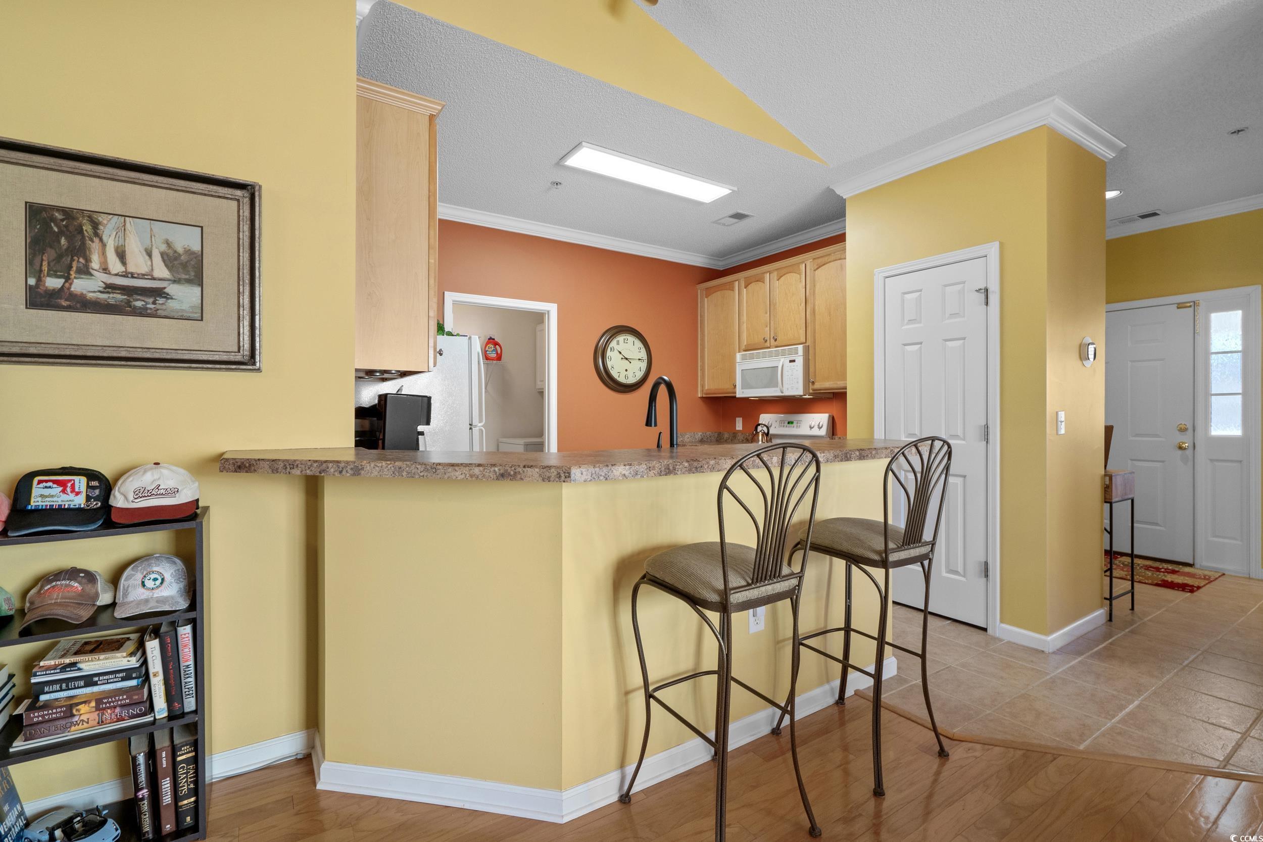 5852 Longwood Drive, Unit 301 Murrells Inlet, SC 29576 - Photo 15 of 35 Kitchen featuring ornamental molding, a kitchen bar, light wood-type flooring, light brown cabinets, and white appliances