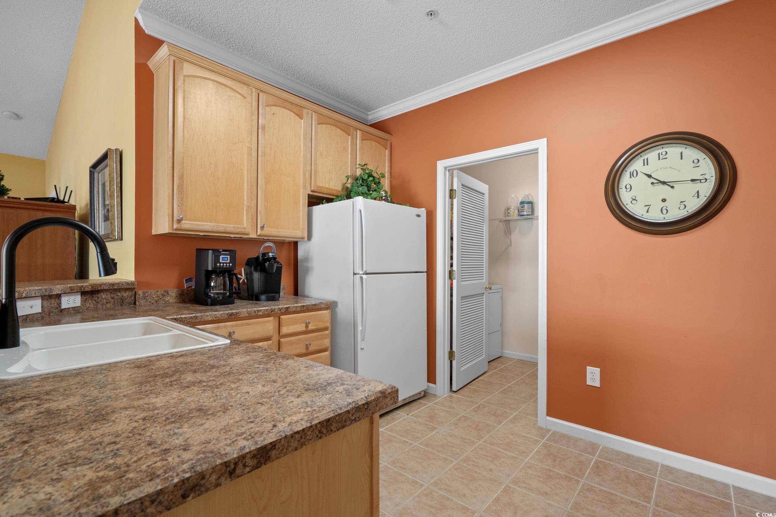 5852 Longwood Drive, Unit 301 Murrells Inlet, SC 29576 - Photo 6 of 35 Kitchen with light brown cabinets, freestanding refrigerator, crown molding, light tile patterned floors, and a textured ceiling