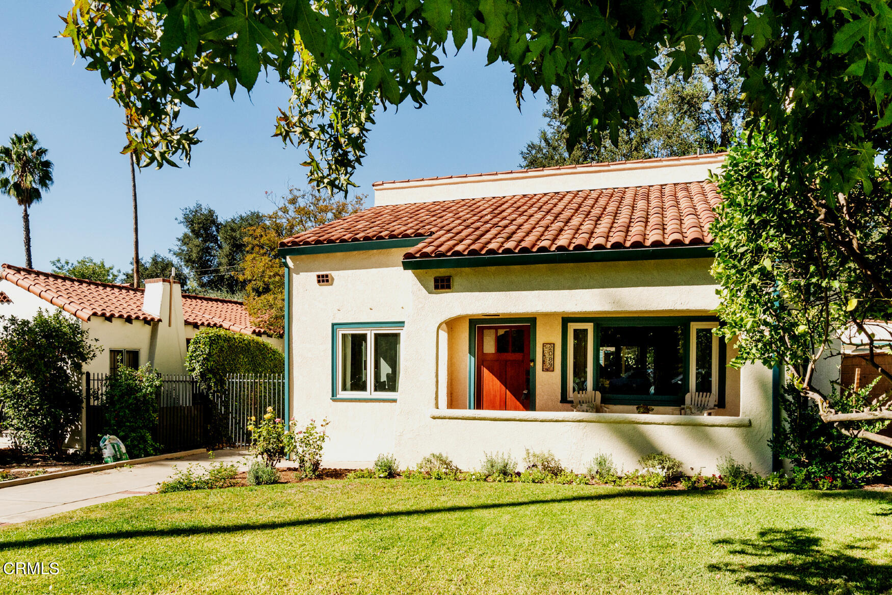 a view of a white house with large windows and a yard with plants and large trees