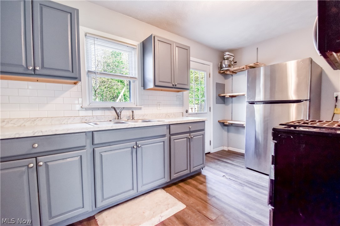 1969 Paisley Road Madison, OH 44057 - Photo 2 of 20 Kitchen featuring gray cabinetry, white subway tile backsplash, a stainless steel refrigerator, wood-finish flooring, and a window above the sink