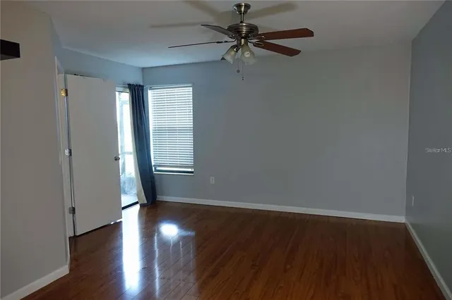 an empty room with wooden floor fan and windows
