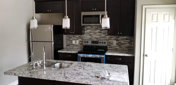 a kitchen with kitchen island granite countertop a refrigerator and a sink
