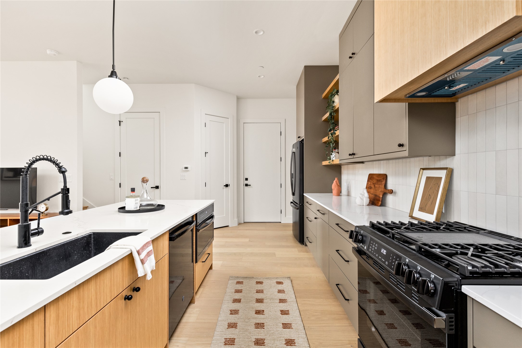 4414 South 1st Street, Unit 3 Austin, TX 78745 - Photo 21 of 39 Two tone kitchen featuring black appliances, hanging light fixtures, light stone counters, light wood-type flooring, and backsplash