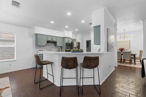 a kitchen with stainless steel appliances kitchen island granite countertop a dining table chairs and a refrigerator