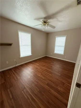 an empty room with wooden floor chandelier fan and windows