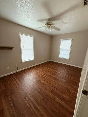 an empty room with wooden floor chandelier fan and windows
