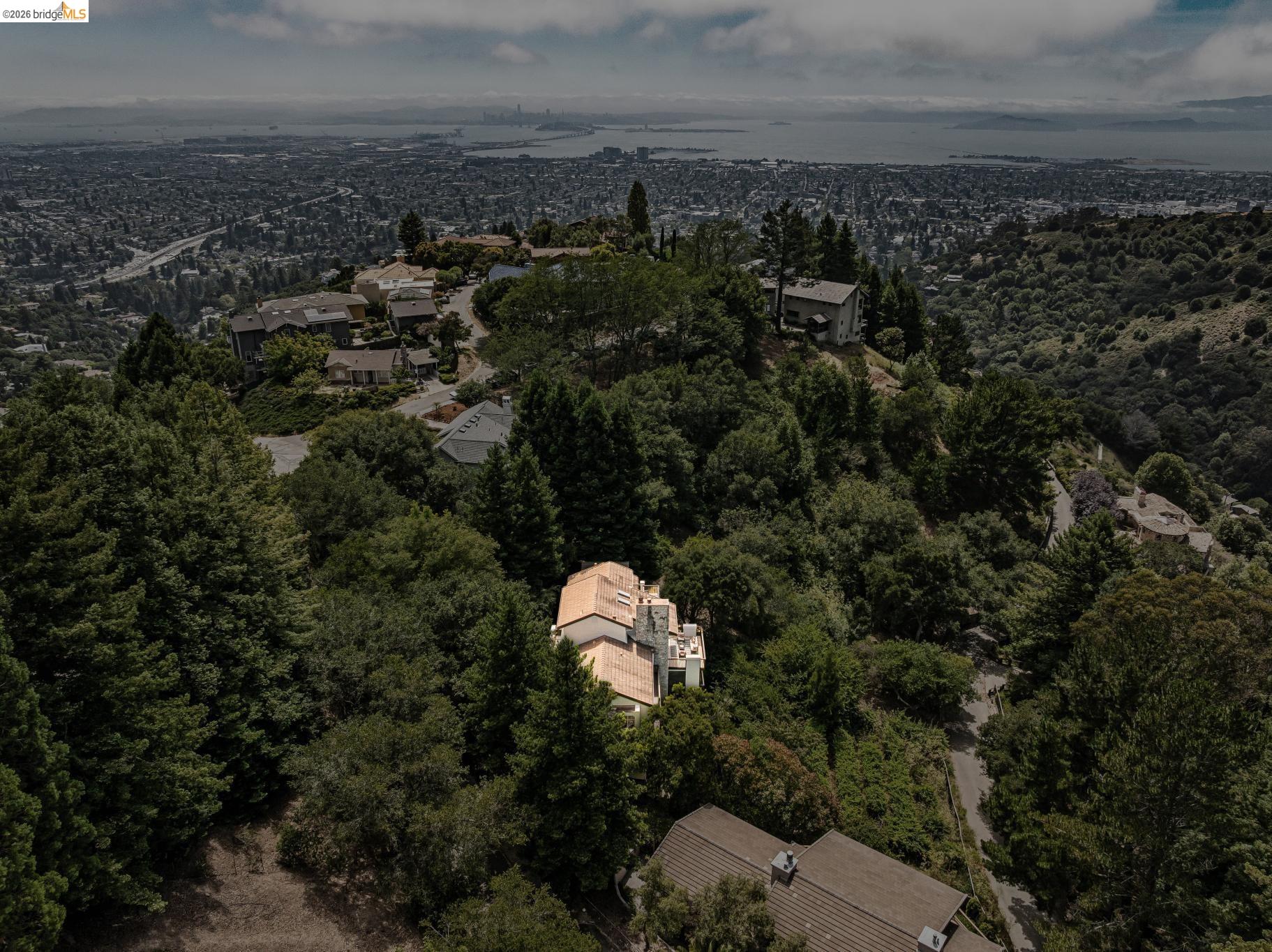 1325 Drury Road Berkeley, CA 94705 - Photo 70 of 71 Aerial perspective showcasing a property nestled within a densely treed hillside, featuring a terracotta tile roof and light-colored exterior walls