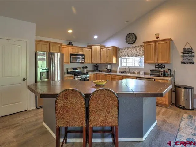 a kitchen with stainless steel appliances granite countertop a stove a sink a refrigerator and chairs