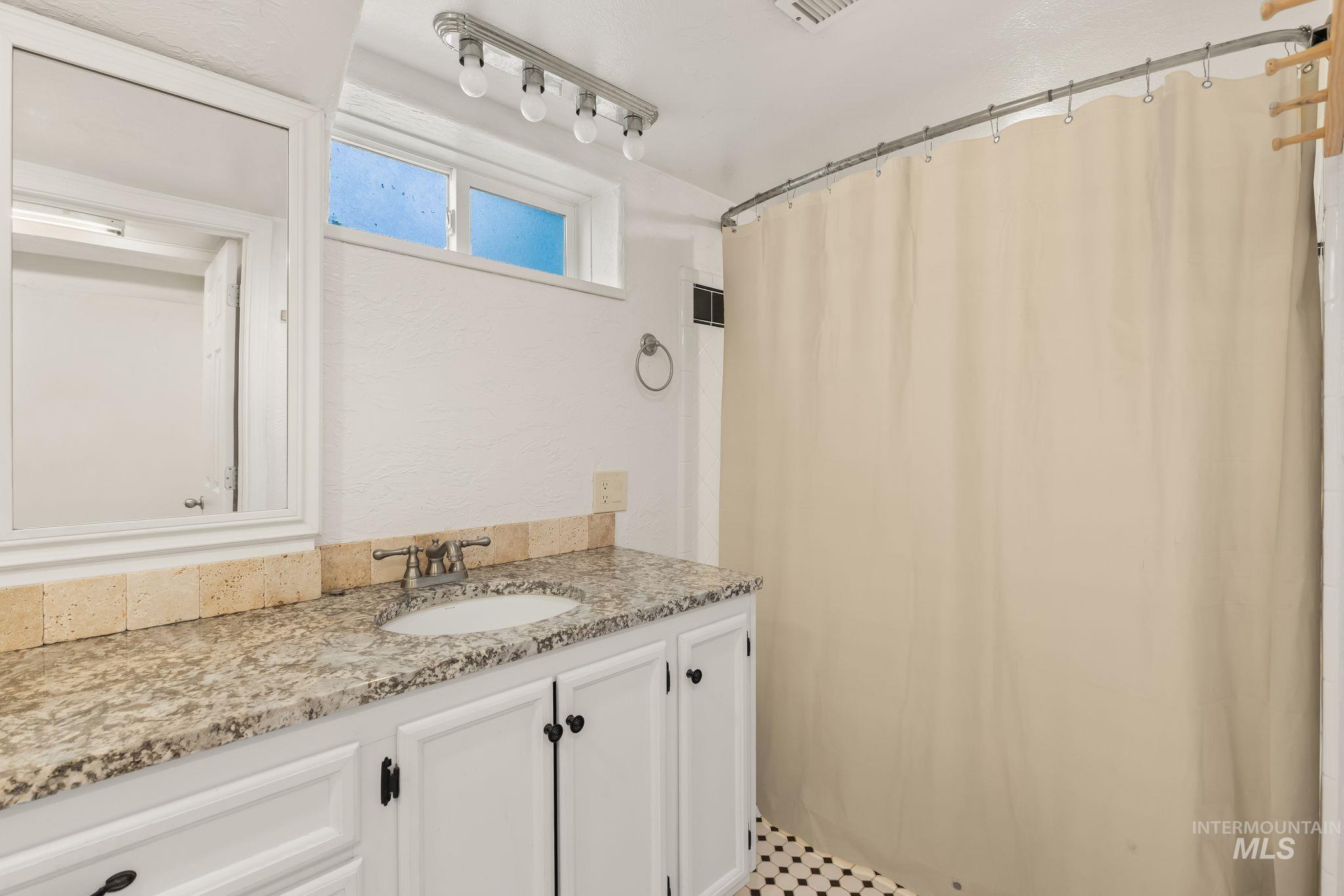 928 3rd Street Clarkston, WA 99403 - Photo 28 of 44 Bathroom featuring a granite-style countertop, white cabinetry with dark hardware, and a black and white tiled floor