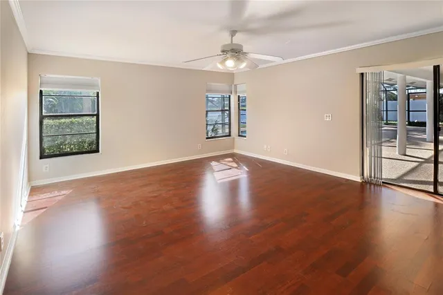 an empty room with wooden floor chandelier fan and windows