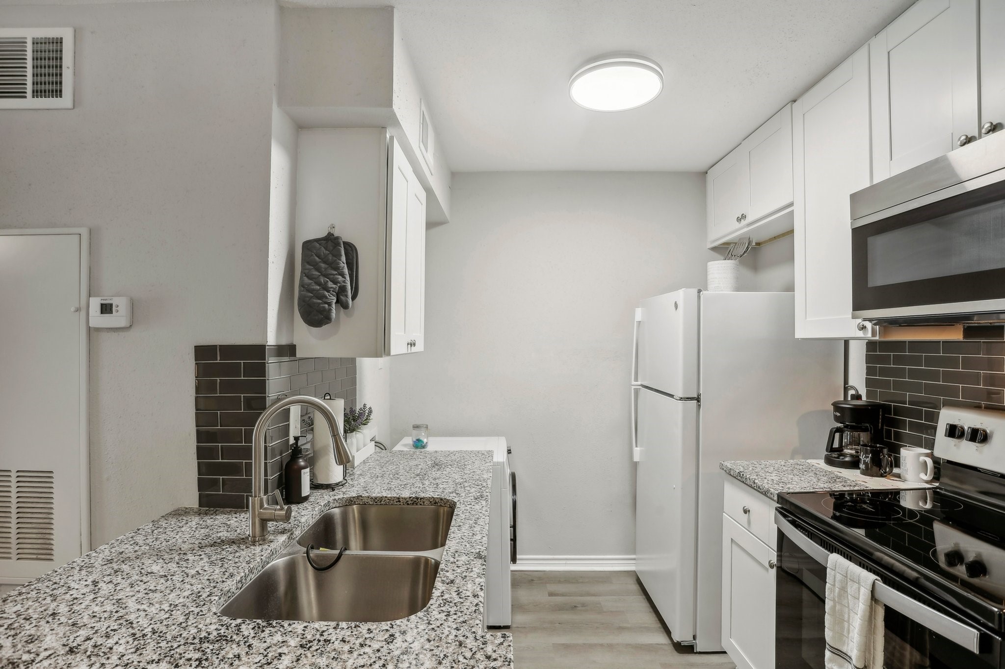 13151 Walden Road, Unit 136 Montgomery, TX 77356 - Photo 7 of 17 This is a modern, compact kitchen with white cabinetry, granite countertops, and stainless-steel appliances, complemented by a sleek, dark tile backsplash. It's well-lit and just right for a one bedroom condo.