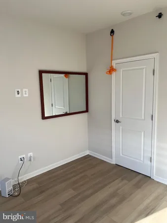 a view of an empty room with wooden floor and a mirror