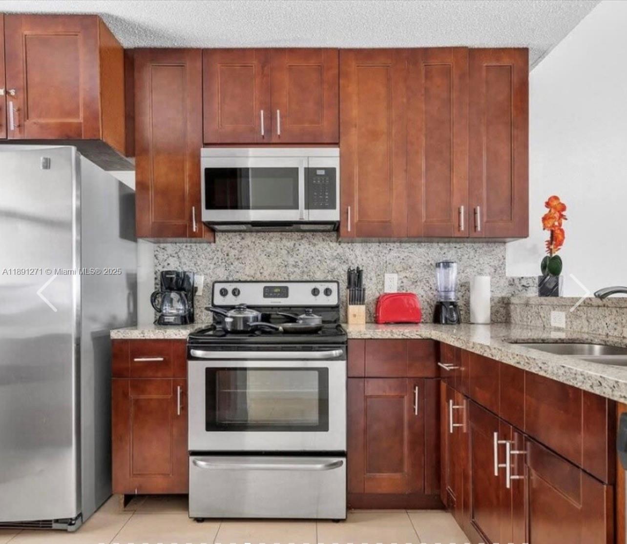 2421 Southwest 58th Manor, Unit 1 Dania Beach, FL 33312 - Photo 6 of 15 a kitchen with stainless steel appliances granite countertop a stove top oven a sink dishwasher and a refrigerator with wooden cabinets