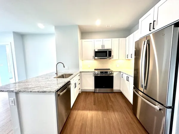 a kitchen with stainless steel appliances granite countertop a refrigerator a sink dishwasher a stove top oven a refrigerator with wooden floor