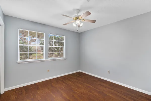 an empty room with wooden floor chandelier fan and windows