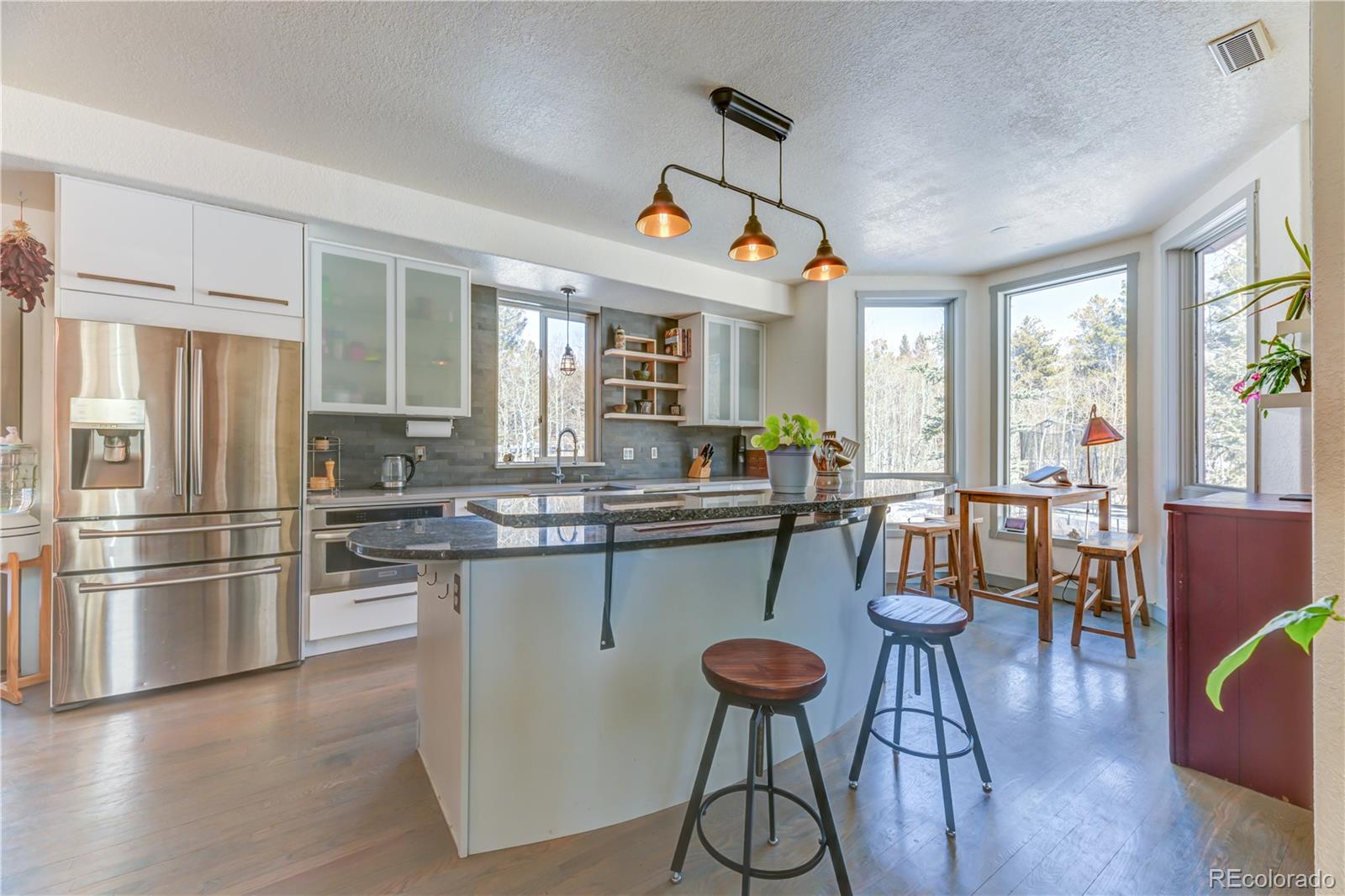 186 Thunder Ridge Road South Nederland, CO 80466 - Photo 16 of 50 a kitchen with stainless steel appliances granite countertop a stove a refrigerator a sink a dining table and chairs with wooden floor