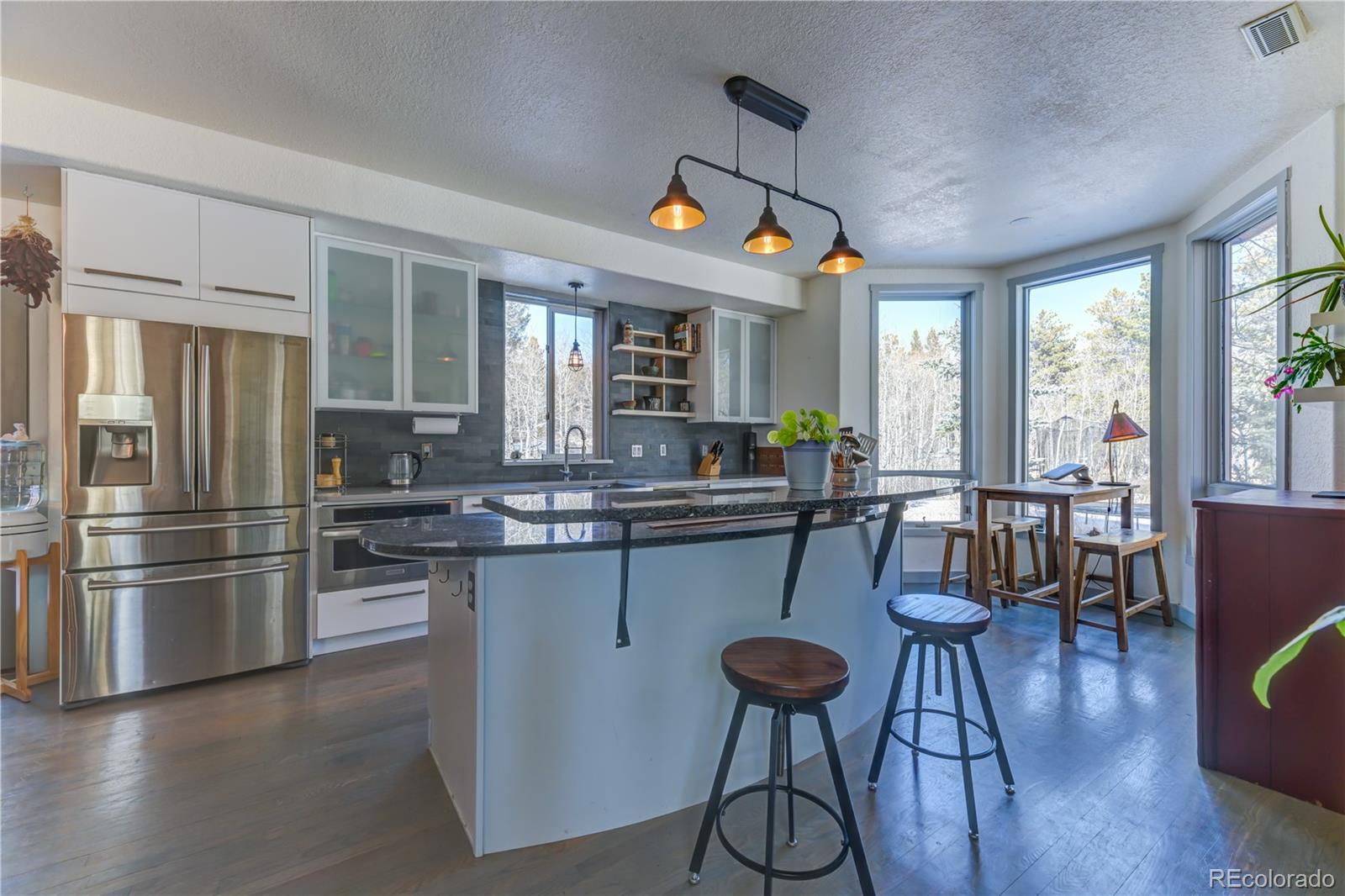186 Thunder Ridge Road South Nederland, CO 80466 - Photo 44 of 50 a kitchen with stainless steel appliances granite countertop a refrigerator a stove a sink dishwasher a dining table and chairs with wooden floor