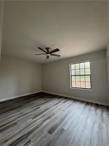an empty room with wooden floor fan and windows