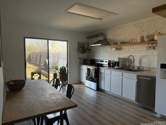 a kitchen with stainless steel appliances granite countertop a stove a refrigerator a sink a dining table and chairs with wooden floor