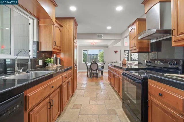 a kitchen with stainless steel appliances granite countertop a stove top oven a sink a dining table and chairs