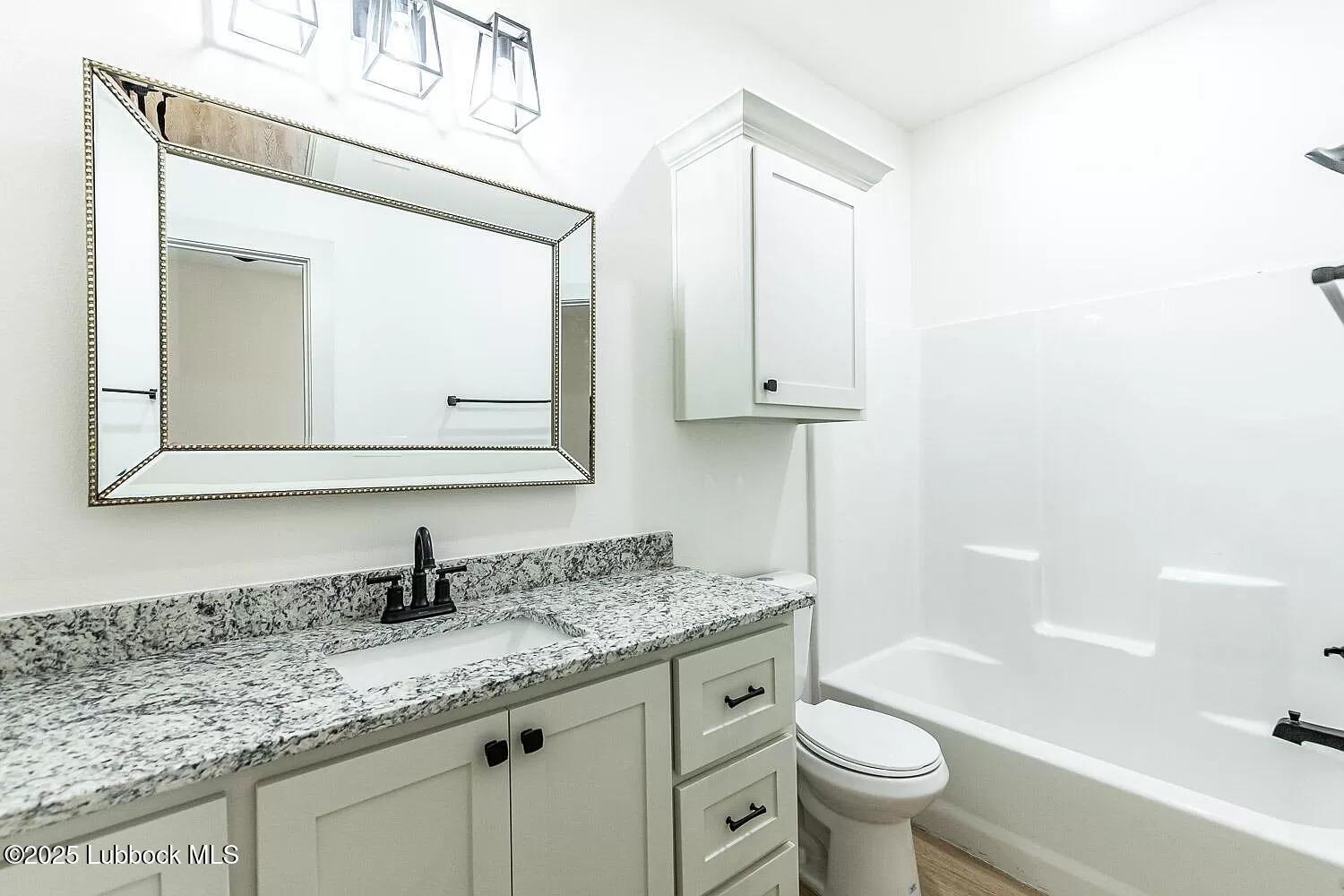 2113 20th Street, Unit A & B Lubbock, TX 79411 - Photo 11 of 31 a bathroom with a granite countertop sink a toilet a mirror and bathtub
