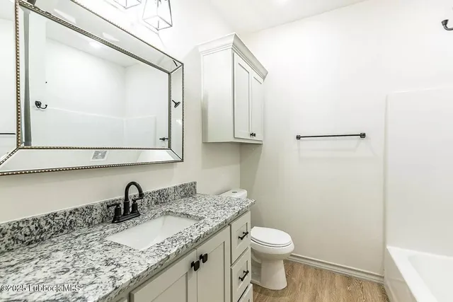 a bathroom with a granite countertop sink vanity mirror and toilet