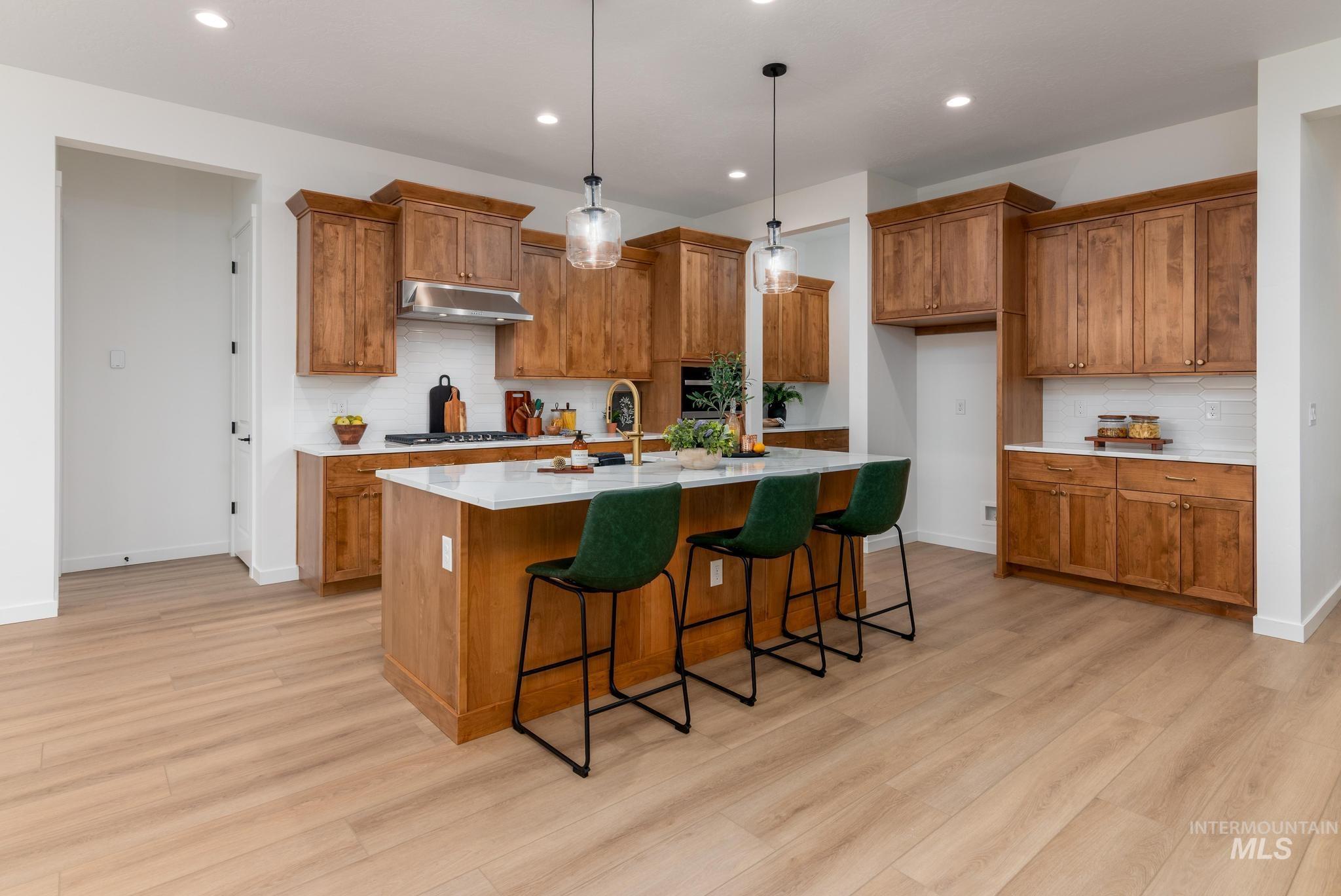 9767 West Nicasio Drive Star, ID 83669 - Photo 5 of 12 Kitchen featuring brown cabinetry, hanging light fixtures, a breakfast bar area, backsplash, and recessed lighting
