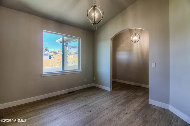 an empty room with wooden floor chandelier and windows