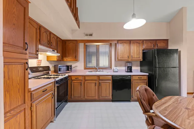 a kitchen with stainless steel appliances granite countertop a refrigerator a sink a stove a dining table and chairs