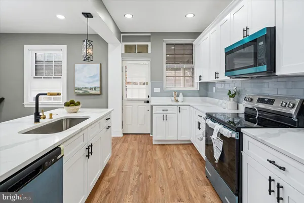 a kitchen with stainless steel appliances a sink dishwasher a stove top oven a refrigerator with wooden floors and cabinets