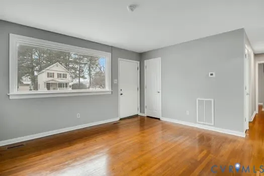 a view of an empty room with wooden floor and a window