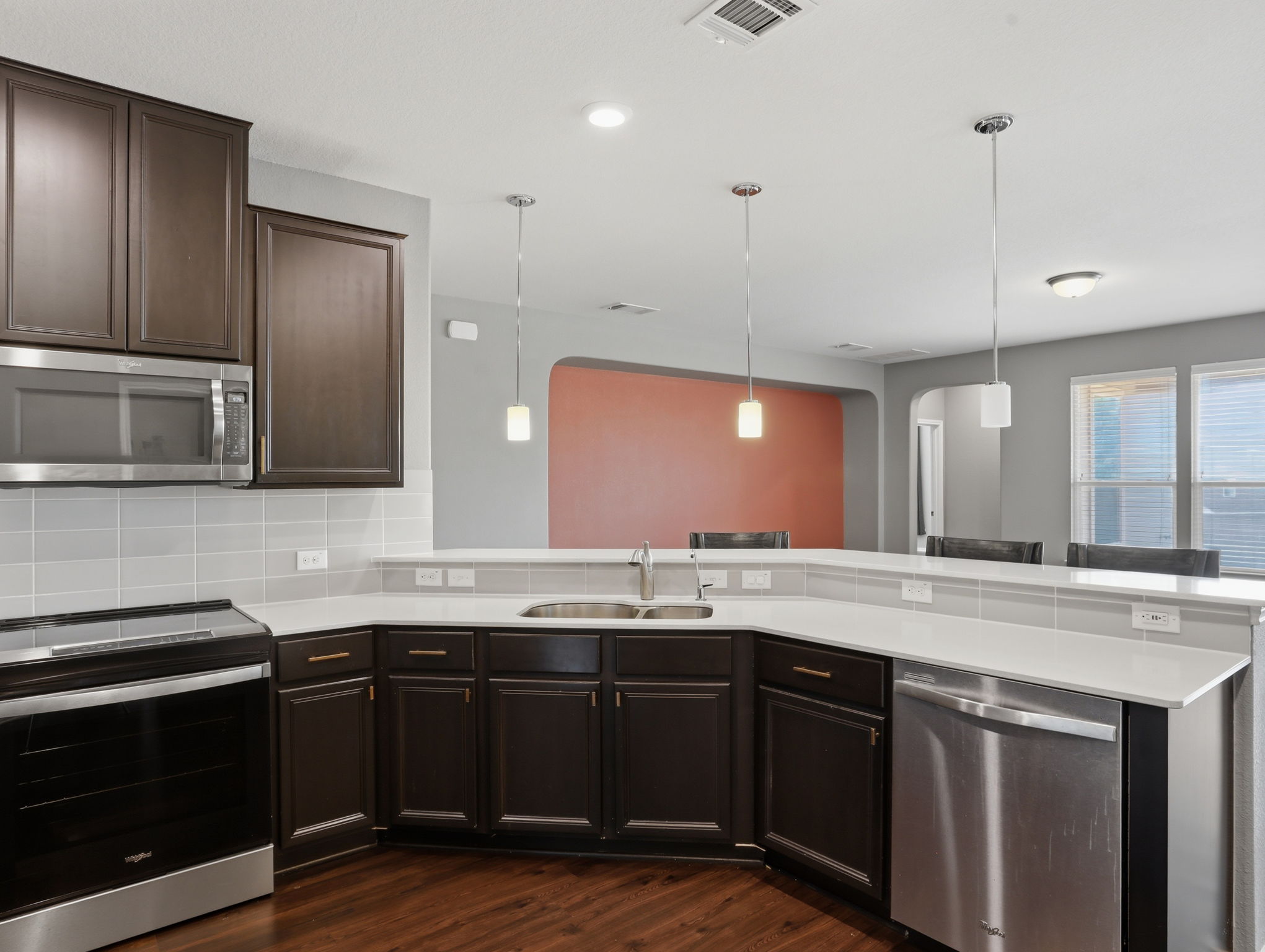 640 Landon Samuel Loop Pflugerville, TX 78660 - Photo 11 of 33 Kitchen featuring dark wood cabinetry, light countertops, stainless steel appliances, a tile backsplash, and three pendant lights