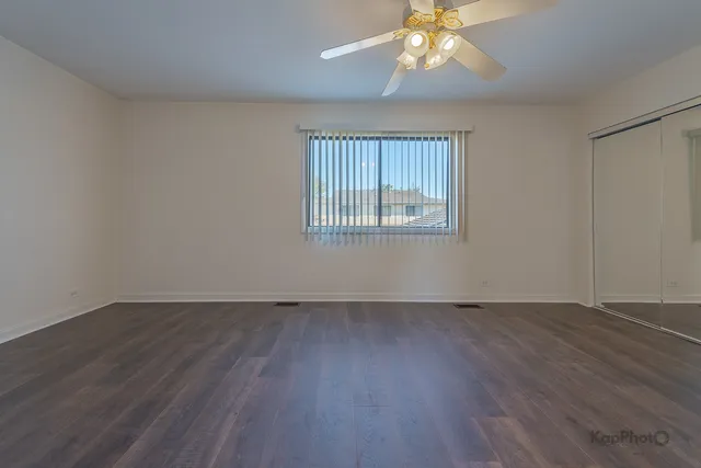 an empty room with wooden floor chandelier fan and windows