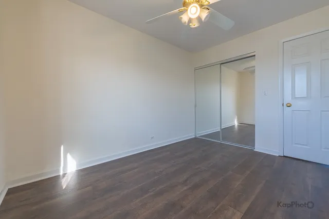 an empty room with wooden floor and a chandelier fan