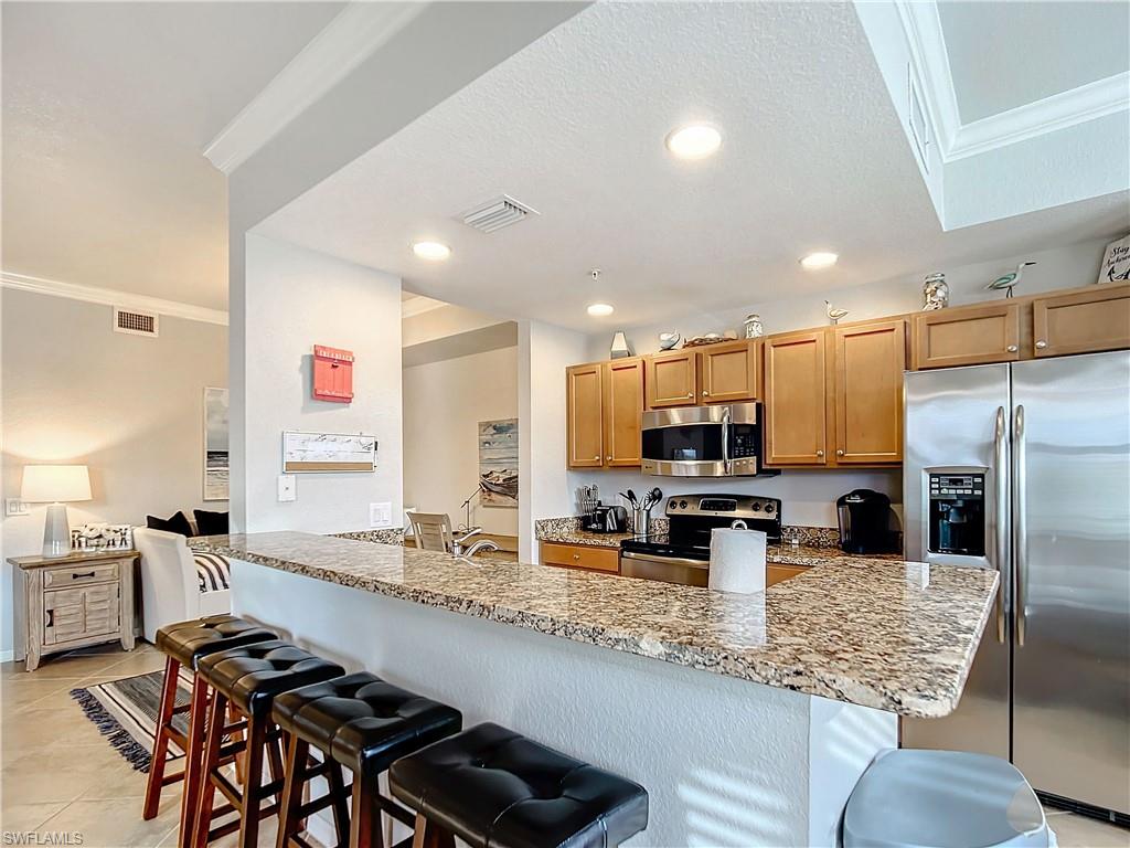 9715 Acqua Court, Unit 127 Naples, FL 34113 - Photo 23 of 50 a kitchen with stainless steel appliances granite countertop a stove top oven a sink a dining table and chairs