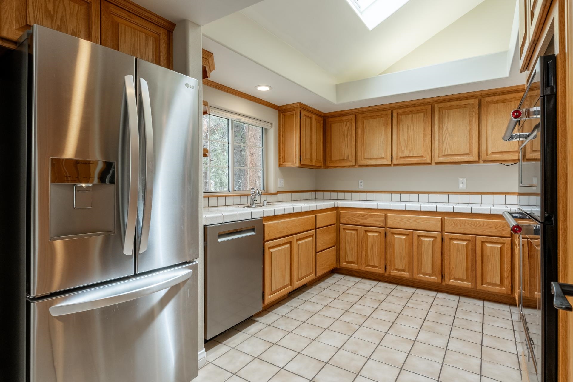272 Ridge Way Mammoth Lakes, CA 93546 - Photo 24 of 55 Kitchen featuring a skylight, wood cabinetry, stainless steel appliances, tile flooring, and a tile countertop with a white tile backsplash