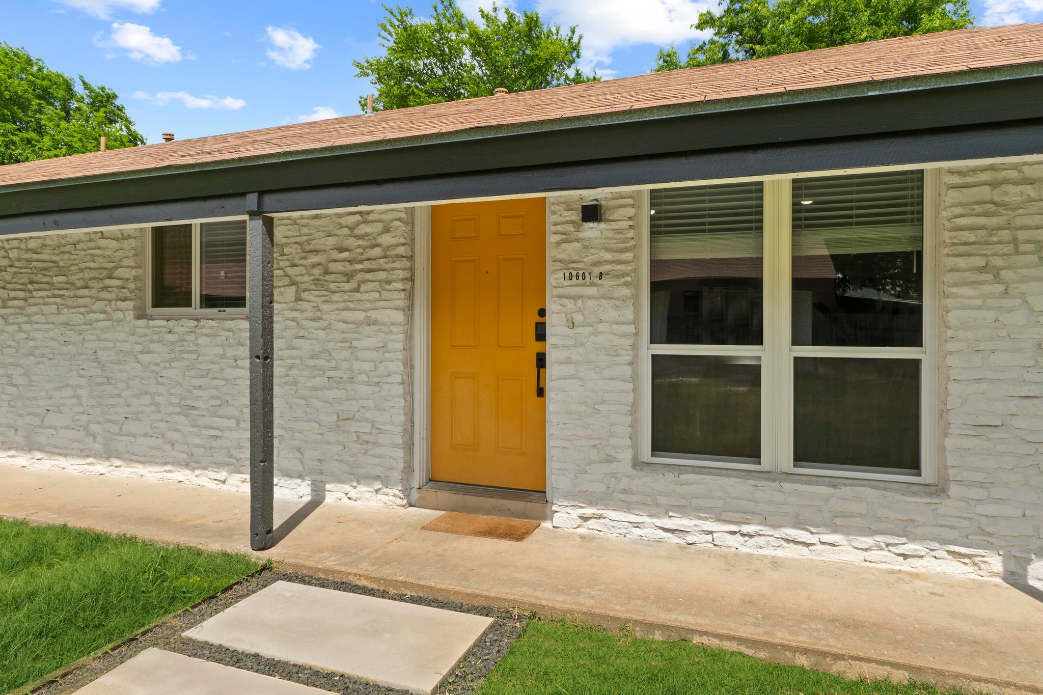 10601 Macmora Road, Unit B Austin, TX 78758 - Photo 2 of 22 A vibrant yellow entry door welcomes you to this home featuring a textured stone facade and covered front porch.