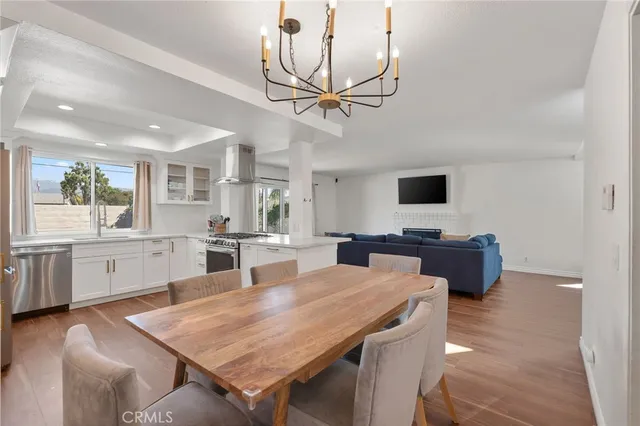 a room with stainless steel appliances kitchen island granite countertop a stove a sink a dining table and chairs with wooden floor