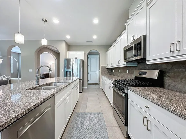 a kitchen with stainless steel appliances granite countertop a sink a stove a refrigerator and chairs