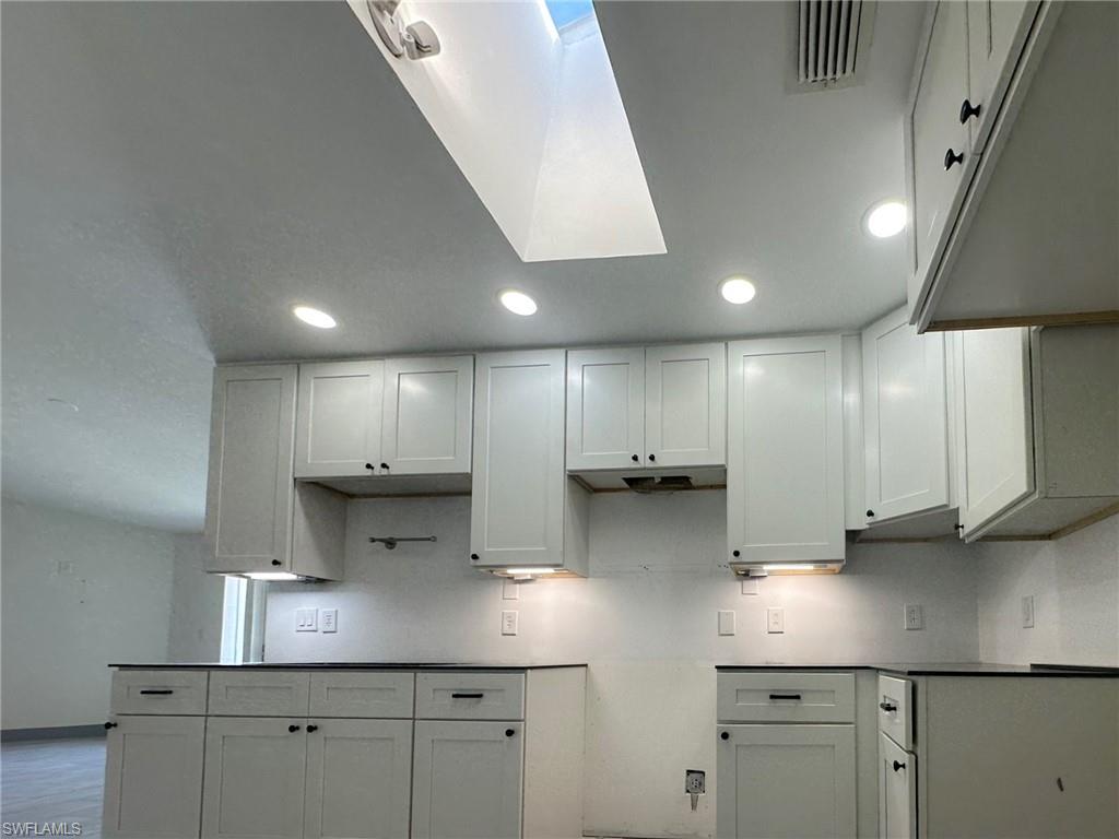 137 Meta Street Fort Myers, FL 33905 - Photo 13 of 50 Kitchen featuring white cabinets, a skylight, under cabinet range hood, and dark countertops