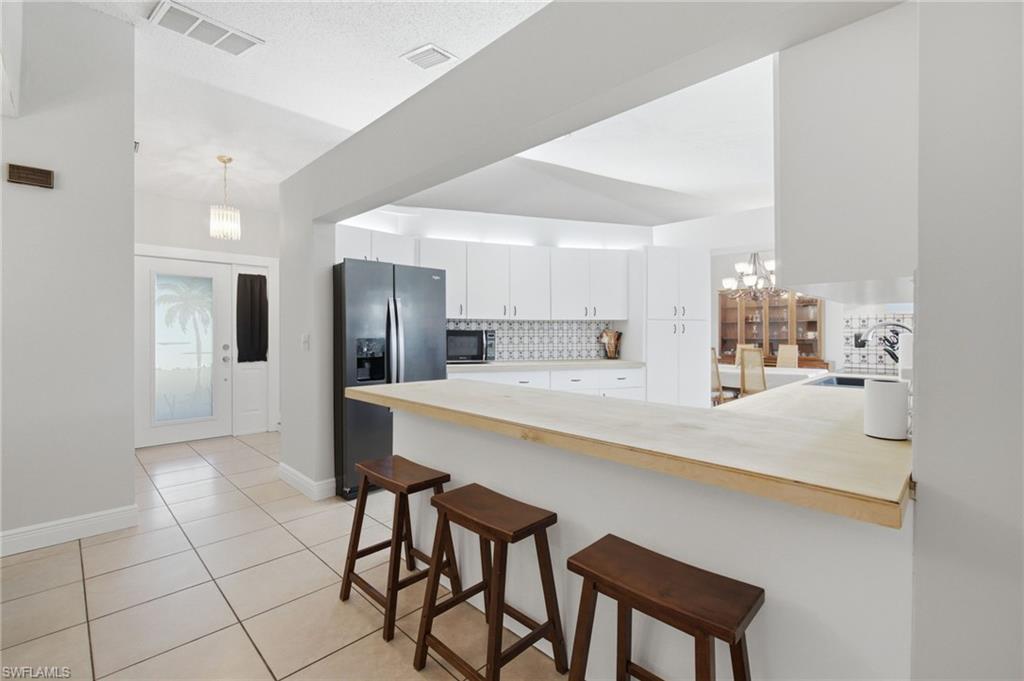 3022 47th Street Southwest Naples, FL 34116 - Photo 13 of 46 Open kitchen with light wood-finish breakfast bar, white cabinetry, and modern tile backsplash