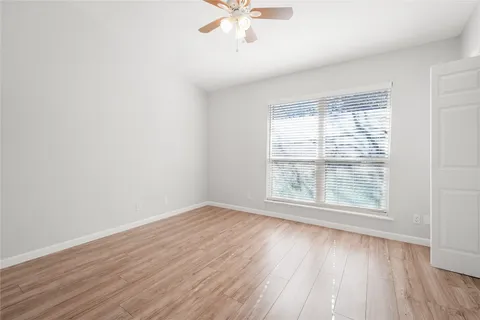 an empty room with wooden floor chandelier fan and windows